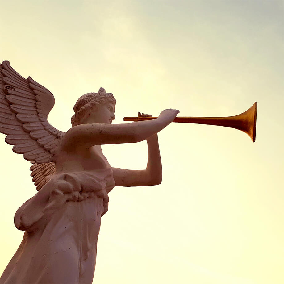 Angel statue blowing a trumpet against a bright sky.