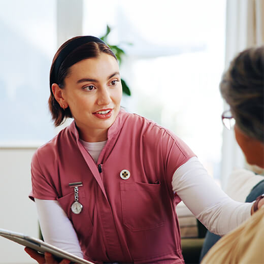 Caregiver in pink scrubs speaking with an older adult.