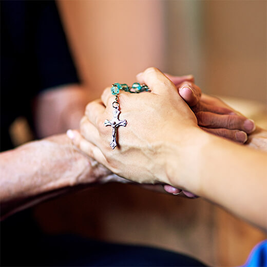 Hands clasped in prayer while holding a rosary with a cross.