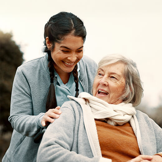 Caregiver smiling with an older woman outdoors.