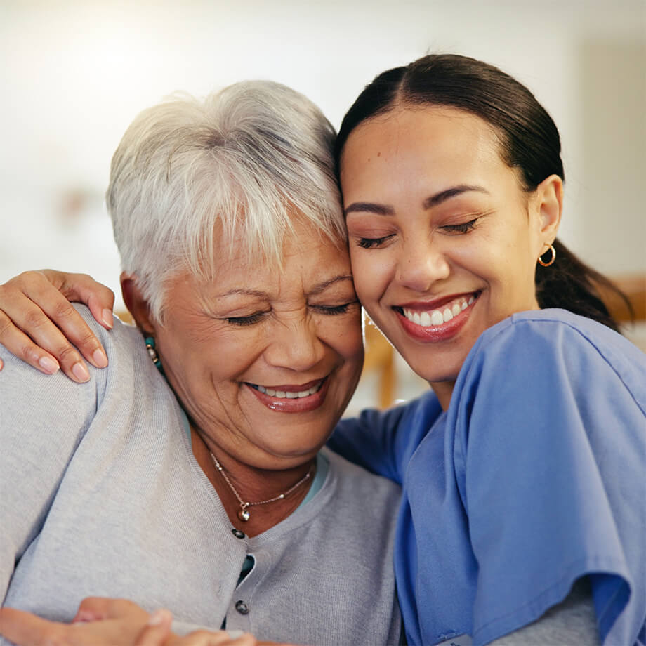 Caregiver smiling while embracing an older woman.